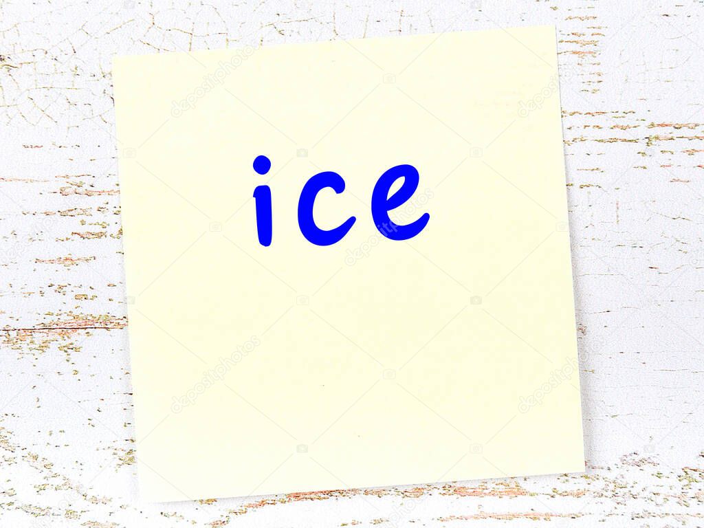Yellow sticky note on wooden wall with handwritten inscription ice
