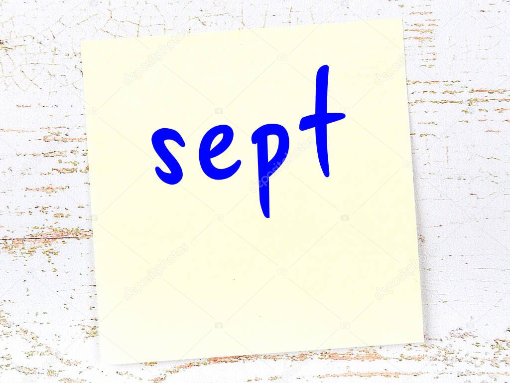Yellow sticky note on wooden wall with handwritten inscription sept