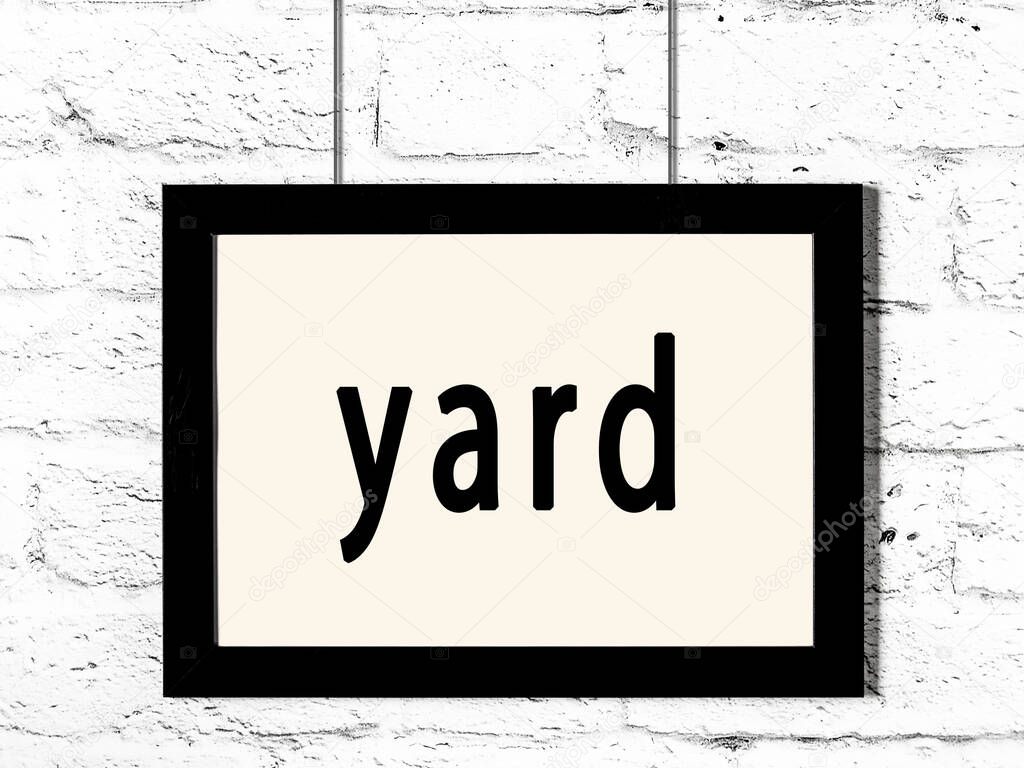 Black wooden frame with inscription yard hanging on white brick wall 