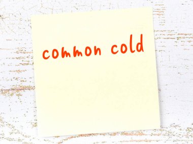 Tahta duvardaki sarı yapışkan notta elle yazılmış soğuk algınlığı yazısı var.