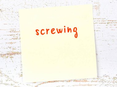 Tahta duvardaki sarı yapışkan notta el yazısıyla yazılmış vida var.