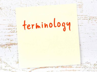 Tahta duvarda el yazısı terminolojisi olan sarı yapışkan bir not.