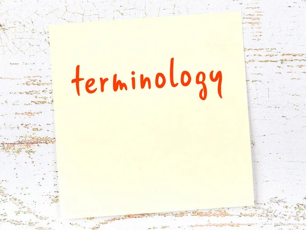 Tahta duvarda el yazısı terminolojisi olan sarı yapışkan bir not.