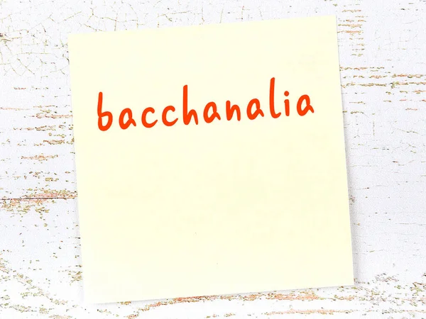 Tahta duvardaki sarı yapışkan notta el yazısıyla yazılmış Bacchanalia.