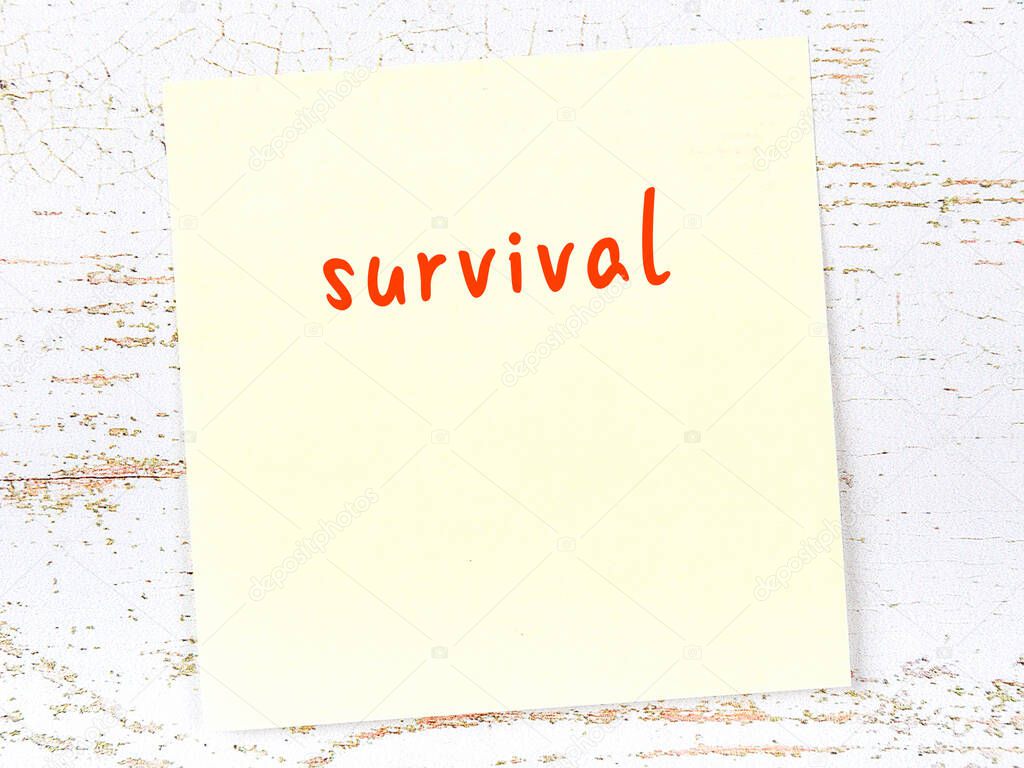 Yellow sticky note on wooden wall with handwritten inscription survival