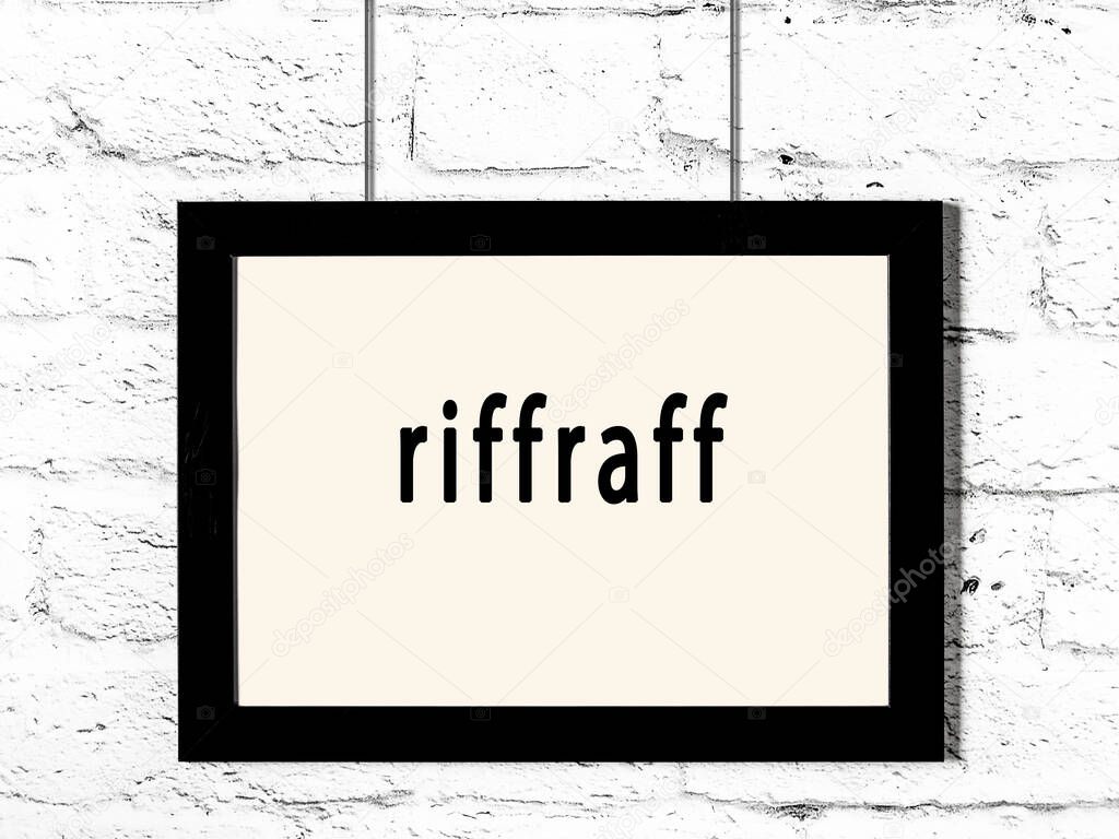 Black wooden frame with inscription riffraff hanging on white brick wall 