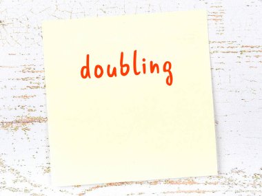 Tahta duvardaki sarı yapışkan notta el yazısıyla yazılmış yazılar iki katına çıkıyor.