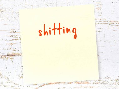 Concept of reminder about shitting. Yellow sticky sheet of paper on wooden wall with inscription