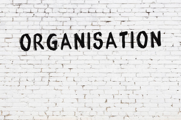 Inscription organisation written with black paint on white brick wall.