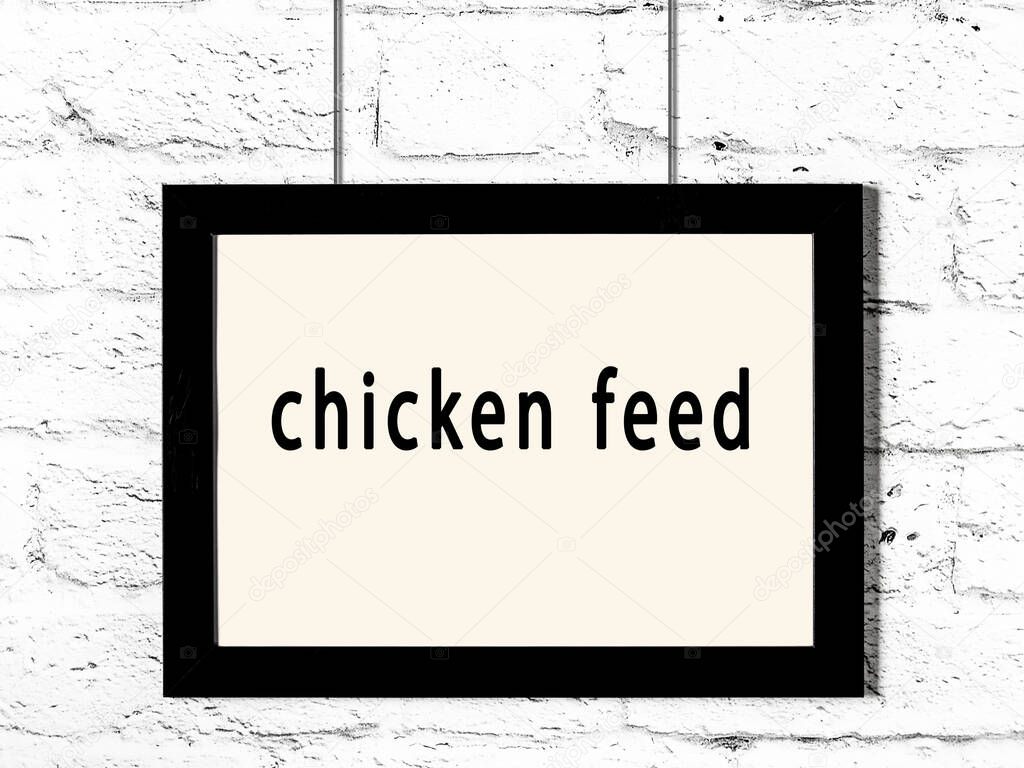 Black wooden frame with inscription chicken feed hanging on white brick wall 