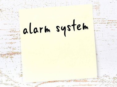 Tahta duvardaki sarı yapışkan notta el yazısıyla yazılmış alarm sistemi var.