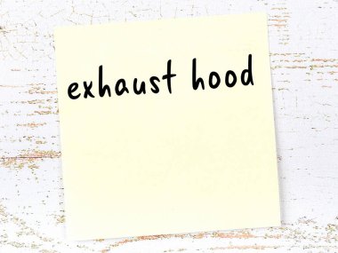 Tahta duvarda el yazısıyla yazılmış egzoz kapağı olan sarı yapışkan bir not.