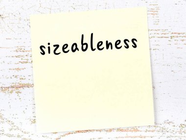 Büyüklükle ilgili hatırlatma kavramı. Tahta duvarda üzerinde yazı olan sarı yapışkan kağıt.