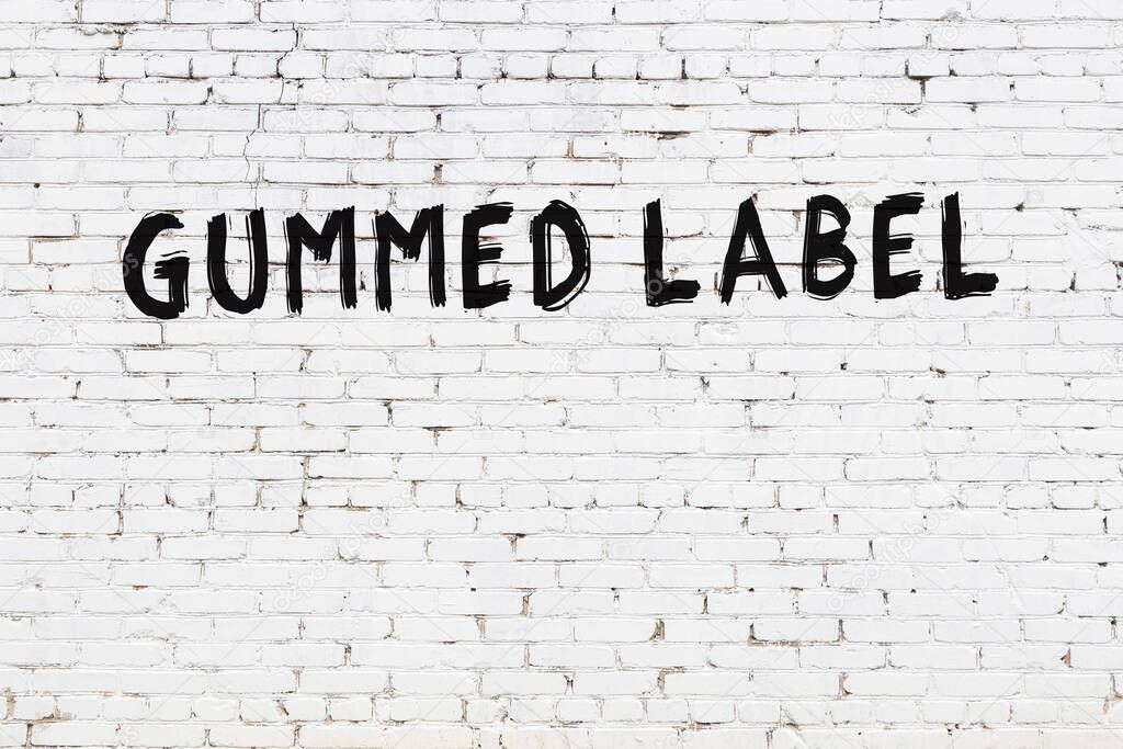 White brick wall with inscription gummed label handwritten with black paint