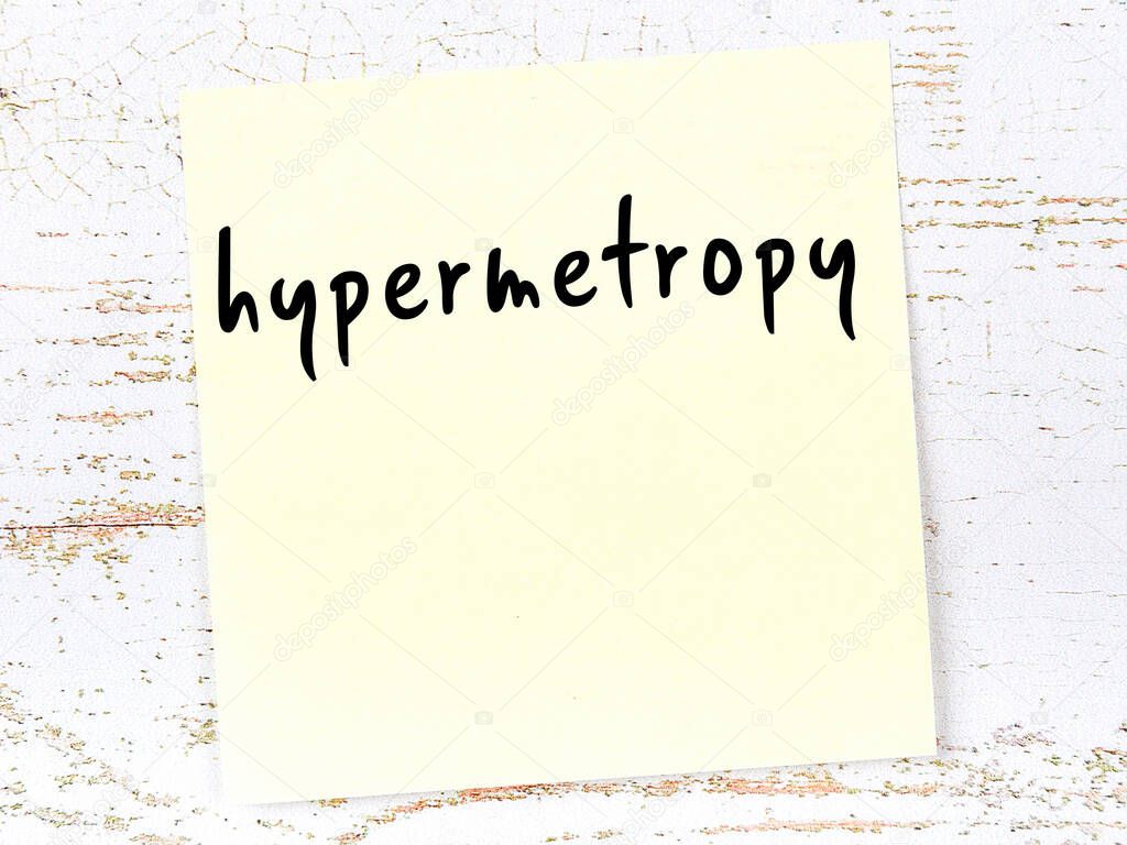 Yellow sticky note on wooden wall with handwritten inscription hypermetropy