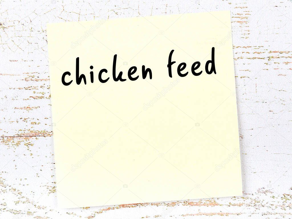 Yellow sticky note on wooden wall with handwritten inscription chicken feed
