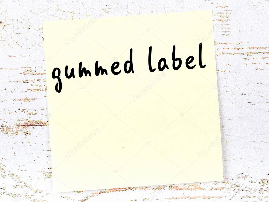 Yellow sticky note on wooden wall with handwritten inscription gummed label