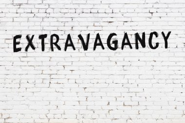 Yazılı beyaz tuğla duvar. Üzerinde siyah boya ile yazılmış savurganlık yazısı var.