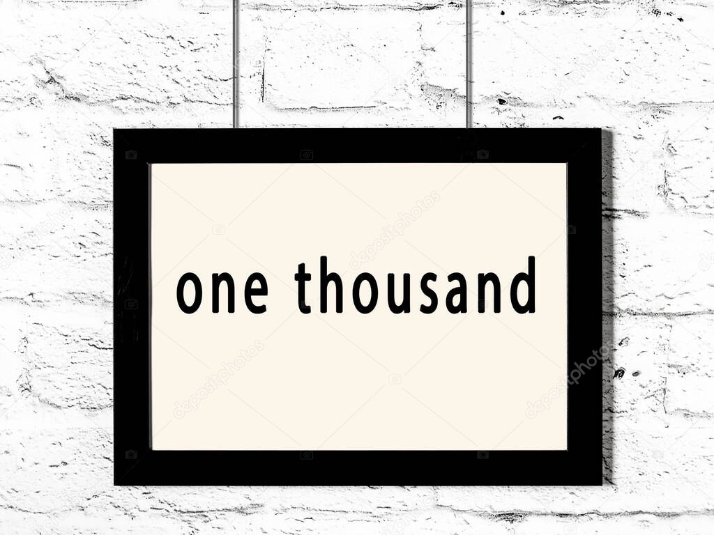Black wooden frame with inscription one thousand hanging on white brick wall 