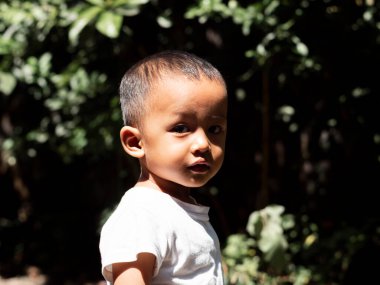 Yakışıklı bir çocuğun yan portresi, beyaz tişörtlü sevimli bir çocuk omzundan kameraya bakıyor, yazın doğal bir geçmişi var. Uzayı kopyala.