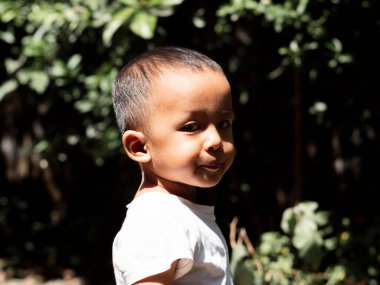 Yakışıklı bir çocuğun yan portresi, beyaz tişörtlü sevimli bir çocuk omzundan kameraya bakıyor, yazın doğal bir geçmişi var. Uzayı kopyala.