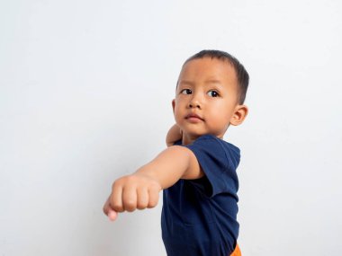 Güçlü ve kararlı Asyalı bir çocuğun portresi. Sıradan tişörtler giyip izole edilmiş beyaz arka planda duruyor. Havayı yumrukluyor ve kameraya güvenle bakıyor.