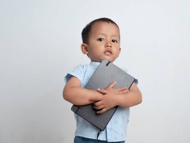 Mutlu sevimli ve neşeli Asyalı çocuk beyaz bir arka planda başının üstünde bir kitap tutuyor. Elinde kitap tutan bir bebek fikri..