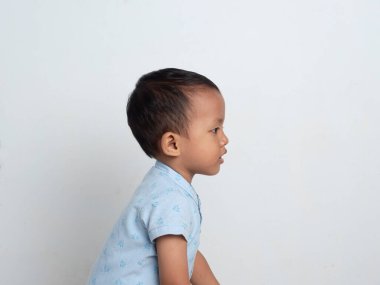 Mavi desenli gömlek giyen Asyalı çocuk beyaz izole arka planda yana bakıyor..