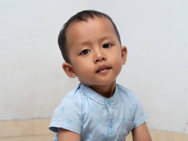 Kameraya bakan tatlı bir Asyalı çocuk. Asyalı çocuk beyaz arka plana karşı kameranın önünde düz poz veriyor..