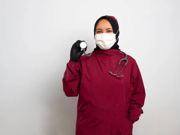 Mutlu Asyalı kadın doktor başörtüsü steteskop kullanıyor ve beyaz arka planda kameraya gülümsüyor..