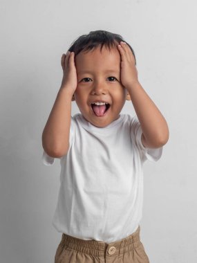 Asyalı çocuk iki eliyle arka planda başını tutarken dilini dışarı çıkartıyor. Yüz ifadeleri, olumlu ve olumsuz duygular. Ad