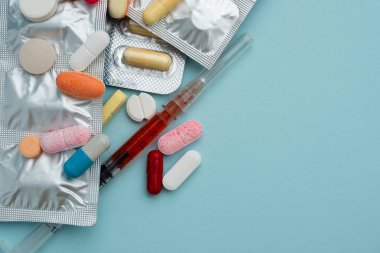 Mavi arka planda çeşitli renkli haplar ve kapsüller, çeşitli ilaçlar, vitaminler, şırınga, steteskop, sağlık ve eczane konseptine katkı maddeleri.