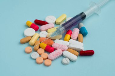 Mavi arka planda çeşitli renkli haplar ve kapsüller, çeşitli ilaçlar, vitaminler, şırınga, steteskop, sağlık ve eczane konseptine katkı maddeleri.