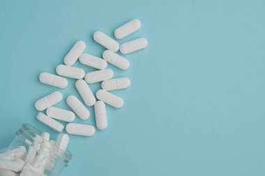 İlaç hapları mavi arka plandaki şeffaf kavanozdan dökülüyor. Sağlık hizmetleri, ilaç tedavileri ve ilaç endüstrisi için idealdir..