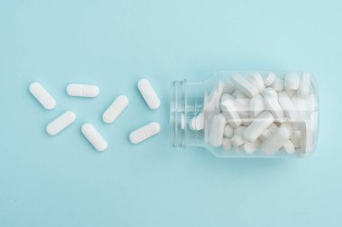 İlaç hapları mavi arka plandaki şeffaf kavanozdan dökülüyor. Sağlık hizmetleri, ilaç tedavileri ve ilaç endüstrisi için idealdir..