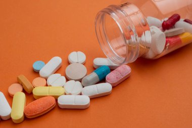 Beyaz kavanoz plastiğinden turuncu arka plana çeşitli renkli antibiyotik kapsülleri dökülmüş. Çeşitli renkli reçeteli kapsül hapları. Sağlık hizmetleri, ilaç tedavileri ve ilaç endüstrisi için idealdir..