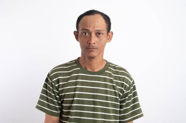 Beyaz çizgili yeşil gömlek giyen ciddi bir adam kameraya yoğun bir şekilde bakıyor ve sert bir yüz ifadesi sergiliyor. Beyaz arka plan odaklanmış ve derin düşüncelere dalmış tavrını vurguluyor..