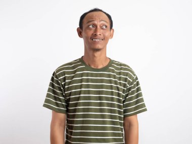 Asyalı bir adam tuhaf ve güvensiz bir gülümseme ile yana bakıyor. Beyaz arka planda günlük hayatta tereddüt, şaşkınlık, merak ve belirsiz duyguları ifade eden sıradan bir portre..