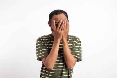 İzole edilmiş beyaz arka planda genç yakışıklı bir adam gözleri kapatıyor ve parmaklarından bakıyor.