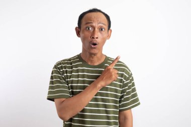 Beyaz çizgili yeşil tişört giyen bir adam sanki bir fikri varmış gibi işaret parmağı havada yukarı bakıyor. Onun ifadesi hareketli ve coşkulu. Açık mavi arka plan onun enerjisini vurguluyor.