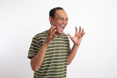 Beyaz çizgili yeşil gömlek giyen Asyalı bir adam kızgın bir ifade sergiliyor, dişlerini gösteriyor ve ellerini pençe gibi hareketlerle kaldırıyor, sanki öfke ya da hüsran içindeymiş gibi. Sade beyaz arkaplan konuyu vurgular.