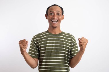 Beyaz çizgili yeşil tişörtlü bir adam kutlama ya da zafer jesti olarak ellerini havaya kaldırıyor..