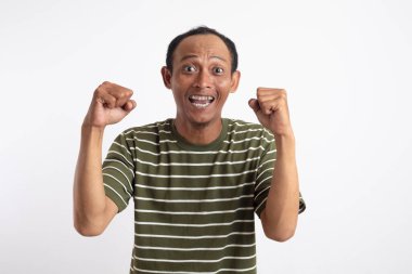 Beyaz çizgili yeşil tişörtlü bir adam kutlama ya da zafer jesti olarak ellerini havaya kaldırıyor..