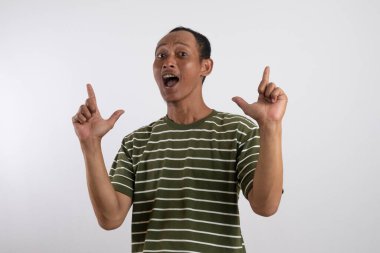 Beyaz çizgili yeşil tişört giyen Asyalı bir adam sağlam sarı bir arka plana güvenerek başparmak sallıyor ve gülümsüyor. Bu resim pozitifliği, onayı ve tatmini resmediyor.