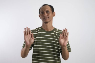 Beyaz çizgili yeşil gömlekli bir Asyalı avucunu ileri doğru uzatarak şaşırmış ve tetikte bir ifadeyle dur işareti veriyor. Düz beyaz arka plan dramasını vurguluyor.
