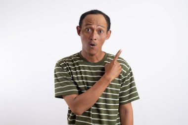 Yeşil tişörtlü Asyalı bir adam, sanki bir reklam aracı için beklenmedik bir şey fark ediyormuş gibi, şaşırmış ve meraklı bir ifadeyle yan tarafı işaret ediyor. Beyaz arka plan onun heyecanlı ifadesini vurguluyor..