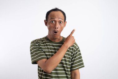 Yeşil tişörtlü Asyalı bir adam, sanki bir reklam aracı için beklenmedik bir şey fark ediyormuş gibi, şaşırmış ve meraklı bir ifadeyle yan tarafı işaret ediyor. Beyaz arka plan onun heyecanlı ifadesini vurguluyor..