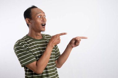 Yeşil tişörtlü Asyalı bir adam, sanki bir reklam aracı için beklenmedik bir şey fark ediyormuş gibi, şaşırmış ve meraklı bir ifadeyle yan tarafı işaret ediyor. Beyaz arka plan onun heyecanlı ifadesini vurguluyor..