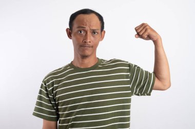 Pozitif Asyalı adamın belden yukarı vuruşu kolunu yukarıda tutuyor. Ne kadar güçlü olduğunu gösteriyor. Gülümsüyor, gururlu bir şekilde beyaz stüdyo arka planında izole edilmiş siyah tişört giyiyor.
