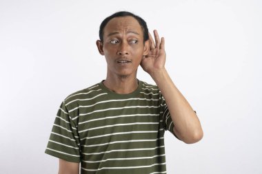 Genç yakışıklı Asyalı adam beyaz arka planda izole edilmiş. Kulağına elini sürerek bir şeyler dinliyor.